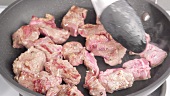Diced beef being fried in a pan