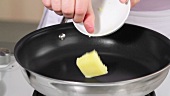 A piece of butter being added to a pan on a hob
