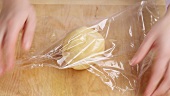 Shortbread pastry being shaped into a ball and wrapped in cling film
