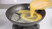 Beaten eggs being added to a pan of melted butter