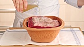 Stock and white wine being added to beef in a terracotta baking dish