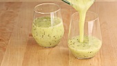 Banana and kiwi smoothie being poured into two glasses
