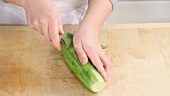 A cucumber being peeled and cut in half lengthways