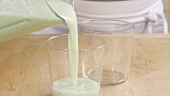 A cucumber and yogurt drink being poured into tow glasses