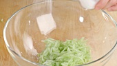 Grated cucumber in bowl being seasoned with salt