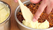 Cottage pie being made: mashed potatoes being placed on top of minced meat