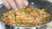 A simmering rice and vegetable stew being seasoned with salt and ground black pepper