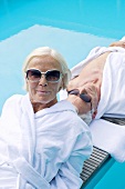 Älteres Paar in Bademänteln auf Holzliege am Swimmingpool