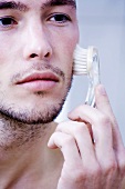 Mann massiert sein Gesicht mit Bürste