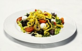 Pasta with pesto on salad leaves with olives, mozzarella and tomatoes