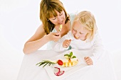 Mother and daughter eating fruit from plate