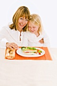 Mother & daughter sitting at table in front of vegetable terrine