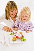 Mother and daughter sitting at table with plate of fruit