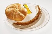 Sausage, bread roll and sachet of mustard on plate