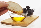 Hand taucht Weissbrotscheibe in Olivenöl