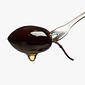 Olive oil dripping from olive on fork