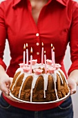 Frau hält Geburtstagsnapfkuchen mit Zuckerguss und Kerzen