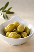 Green olives in small dish in front of olive sprig