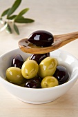 Green and black olives in small dish and on wooden spoon