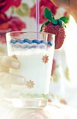 Close-up of woman's hand holding glass of milk with strawberry