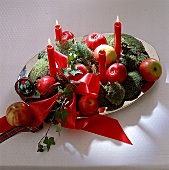 Adventsgesteck mit roten Kerzen, Äpfeln, Moos, Efeu und rotem Band