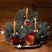 Adventsgesteck mit drei gelben Kerzen auf Äpfeln, Silbersterne