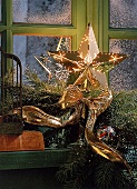 Adventsgesteck mit Goldstern auf Fensterbank, beleuchtet