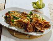 Asian noodles and marinated pork garnished with mint leaves on oval plate