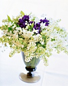Bouquet of lilac, allium daffodils, lilies and violets in vase on white background