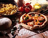 Pizza, Pasta, Brot u. Zutaten liegen auf mehlbestäubten Cotto-Fliesen