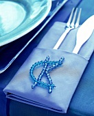 Initialen "CK" aus blauen Perlen auf einer blauen Serviette mit Besteck