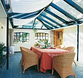 Conservatory house with glass roof, wooden door and wicker furniture
