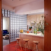 Wand aus Glasbausteinen, kleine Holz küche, 3 Hocker vor d. Tresenbereich