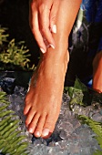 Frau reibt sich Fuß und Bein mit Eis würfel ab, Fuß und Hand sichtbar