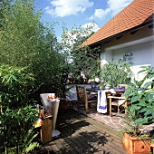 Terrasse mit Gartenmöbeln aus Holz, Büschen und Grill