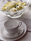 Elegantes Kaffeegedeck in Weiß vor einer Glasschale mit Rosenblüten