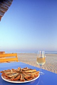 Tapas: Fritierte Sardinen und ein Glas Sherry auf e. Tisch am Strand