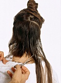 Rear view of woman getting a haircut with metal scissors