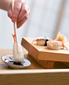 Der fertige Nigiri-Sushi Ebi wird mit Stäbchen in Sojasauce getaucht
