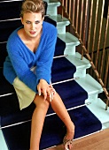 Frau sitzt auf blauer Treppe, blaue Wolljacke, cremefarbener Rock