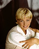 Pretty blonde woman with short hair sitting with hands crossed on shoulders, smiling