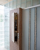 Leicht geöffneter Badezimmerschrank, beklebt mit Marmormosaiksteinchen.