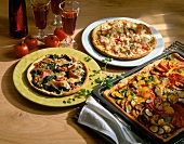 Two different pizzas on plate and one on baking sheet on wooden table