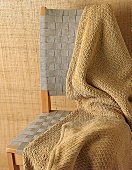 Honigfarbene Decke auf Stuhl mit geflochtener Rücken/Sitzlehne.