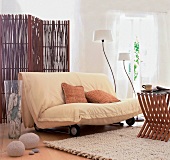 helles Sofa,dahinter ein Paravant aus Weidengeflecht,helle Vorhänge