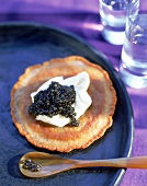 Blini mit Crème Fraiche und Kaviar auf einem blauen Teller angerichtet