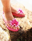 Close-up of woman's feet wearing pink flip flops with fabric flower on it