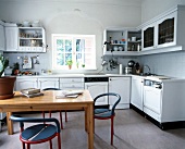 Interior of white kitchen with maple cabinets, blue-red two chairs and table