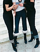 Three women wearing black boots, capri and ankle length pants looking at card