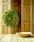 Lush wreath hanging on wooden door and dried hydrangeas on table with bowl